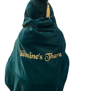 May include: A dark green velvet hooded cape with a gold tassel and the text "Yassine's Thara" embroidered in gold.