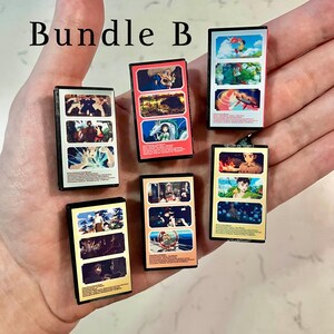 May include: A collection of miniature anime-themed art pieces, each with a black frame and colourful illustrations. The text "Bundle B" is at the top. The pieces feature various scenes and characters from anime.