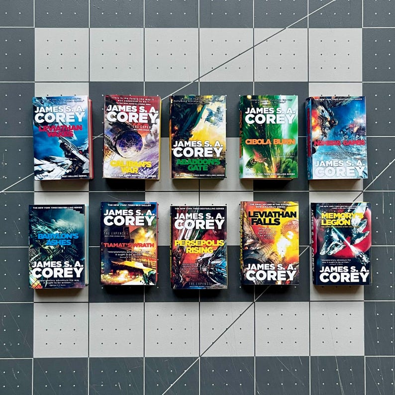 Op de afbeelding: Een verzameling van tien sciencefictionromans van James S.A. Corey, met kleurrijke covers en futuristische afbeeldingen. De boeken zijn gerangschikt op een grijs en wit geblokt oppervlak, met de titels en de naam van de auteur.