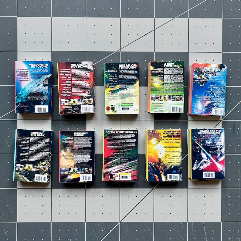 Op de afbeelding: Een verzameling van tien miniatuurboeken met kleurrijke covers en titels als "Welcome to the Future" en "Break On Through." De boeken zijn gerangschikt op een grijs en wit geblokt oppervlak, waarbij hun levendige ontwerpen en tekst worden getoond.