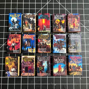 May include: A collection of 14 miniature hardcover books with colorful covers featuring fantasy illustrations and titles like "The Eye of the World", "The Great Hunt", "Dragon Reborn", "The Shadow Rising", "The Fires of Heaven", "Lord of Chaos", "Crown of Swords", "The Path of Daggers", "Winter's Heart", "Crossroads of Twilight", "Knife of Dreams", "The Gathering Storm", "Towers of Midnight", "A Memory of Light", and "New Spring".