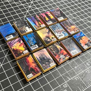 May include: A collection of 15 miniature books with colorful covers and spines. The books are arranged in rows, with the spines facing the viewer. The books are all different sizes and shapes, and they have a variety of designs.