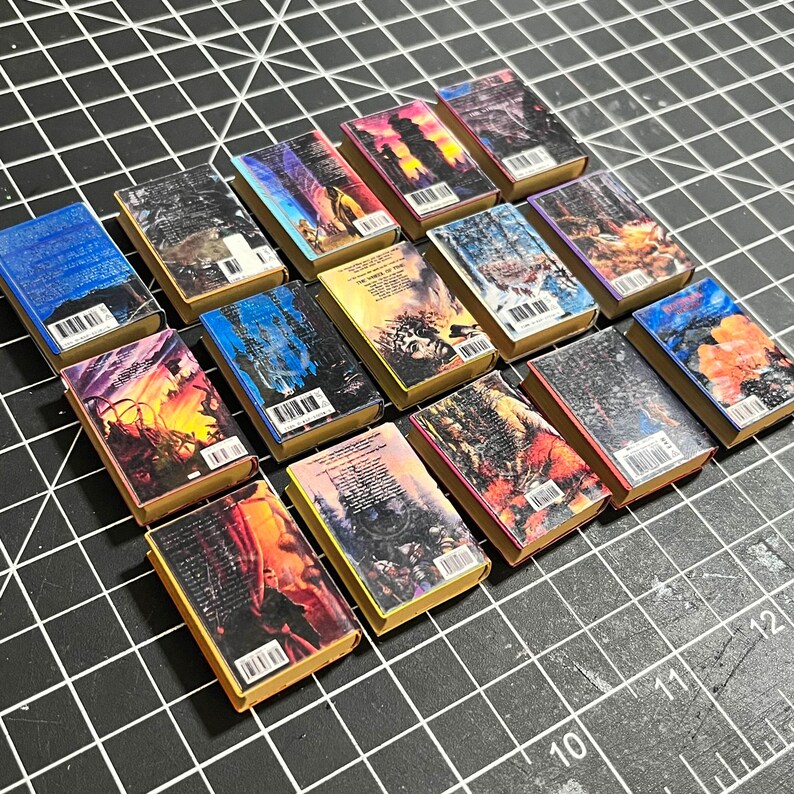 May include: A collection of 15 miniature books with colorful covers and spines. The books are arranged in rows, with the spines facing the viewer. The books are all different sizes and shapes, and they have a variety of designs.