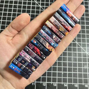 May include: A collection of miniature fantasy novels, including "The Wheel of Time", "The Lord of the Rings", and "A Song of Ice and Fire", displayed on a hand.