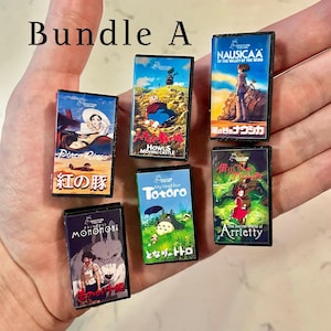 May include: A selection of miniature film cases, each showcasing animated movie titles with vibrant artwork and Japanese text. The cases feature films such as "Nausica&auml; of the Valley of the Wind", "Howl's Moving Castle", "My Neighbor Totoro", "Princess Mononoke", "Porco Rosso", and "The Secret World of Arrietty".