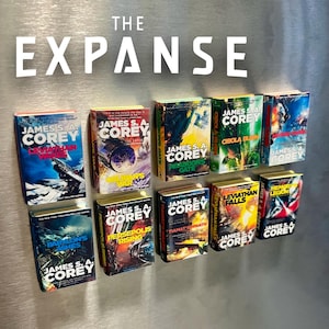 Op de afbeelding: Een verzameling miniatuur boekenmagneten uit de serie "The Expanse" van James S.A. Corey. De kleurrijke covers tonen titels als "Abaddon's Gate" en "Babylon's Ashes". Het woord "EXPANSE" staat in grote witte letters.