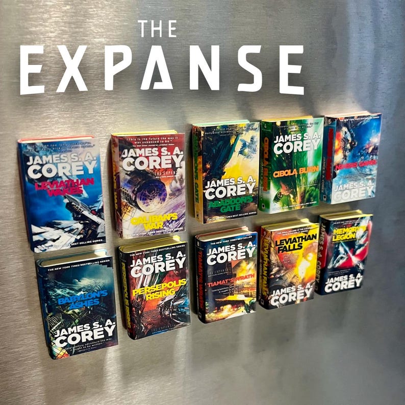 Op de afbeelding: Een verzameling miniatuur boekenmagneten uit de serie "The Expanse" van James S.A. Corey. De kleurrijke covers tonen titels als "Abaddon's Gate" en "Babylon's Ashes". Het woord "EXPANSE" staat in grote witte letters.