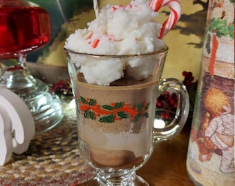 Könnte beinhalten: Eine Glas-Tasse mit einem weißen und roten Zuckerrohr oben drauf, gefüllt mit einer weißen und braunen, geschichteten Kerze. Die Tasse hat ein grünes und rotes Weihnachtsmotiv.