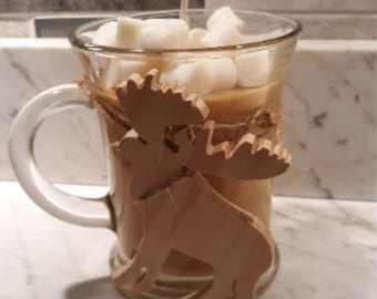 Könnte beinhalten: Eine Kerze in Form einer Glas-Kaffeetasse mit einem braunen Elch-Design an der Seite. Die Kerze ist mit braunem Wachs und weißen Marshmallows gefüllt.