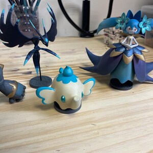 May include: Four hand-painted figurines, including a blue and black winged creature, a blue and gold female figure, a white elephant with blue accents, and a gray and gold figure.