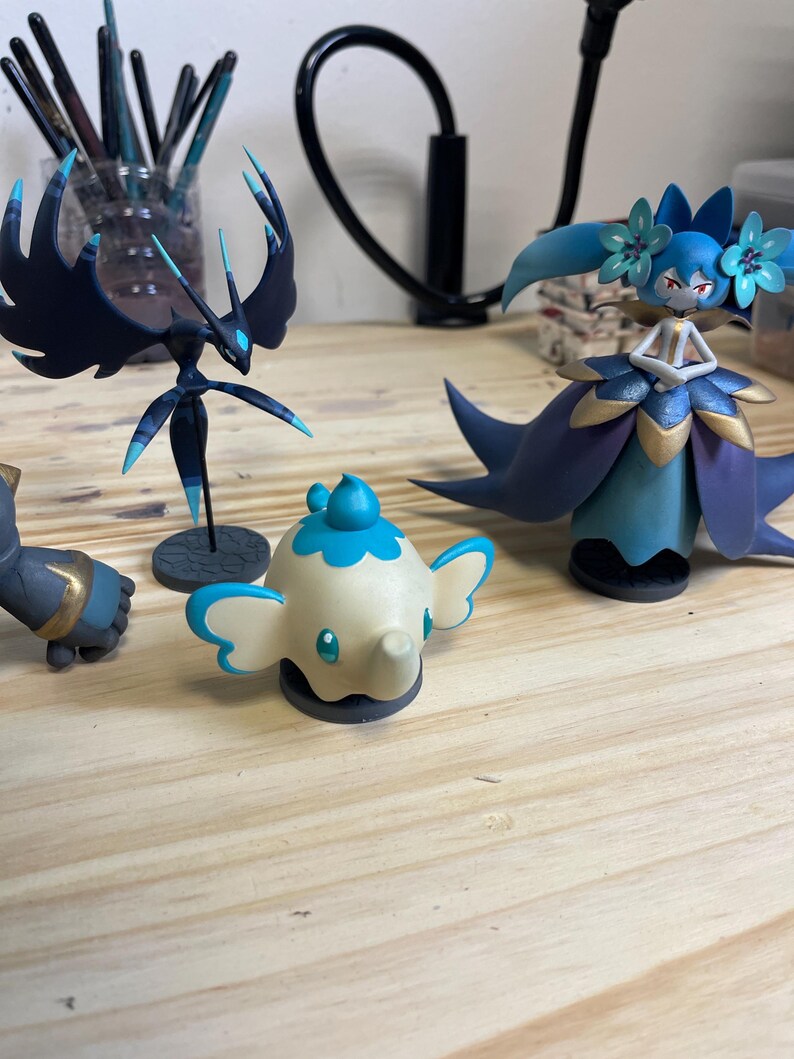 May include: Four hand-painted figurines, including a blue and black winged creature, a blue and gold female figure, a white elephant with blue accents, and a gray and gold figure.