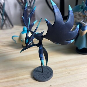 May include: A black and blue detailed figurine of a creature with long, pointed appendages and a base. The creature has a dark blue body with light blue accents and a black base.