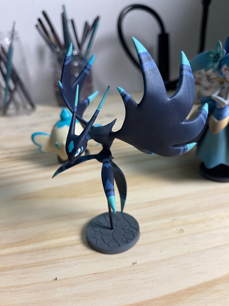 May include: A black and blue detailed figurine of a creature with long, pointed appendages and a base. The creature has a dark blue body with light blue accents and a black base.