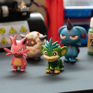 May include: Four colorful figurines, including a pink and white creature with large ears, a white sheep, a green monkey with a leafy head, and a blue creature with a horn. The figurines are made of plastic and are about 4 inches tall.