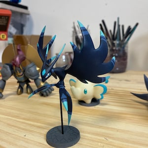 May include: A dark blue and teal colored figurine of a mythical creature with large wings and sharp points. The figurine is standing on a gray base.