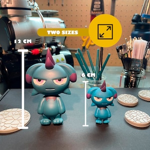 May include: Two teal blue cartoon figures with purple horns and angry expressions. The figures are standing on white bases with a textured design. The larger figure is 12 cm tall and the smaller figure is 6 cm tall. "TWO SIZES" is written in yellow on a black background.