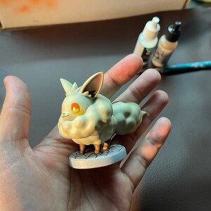 May include: A white and gray Pokemon figurine of a fluffy, fox-like creature with orange eyes. The figurine is standing on a round, gray base.