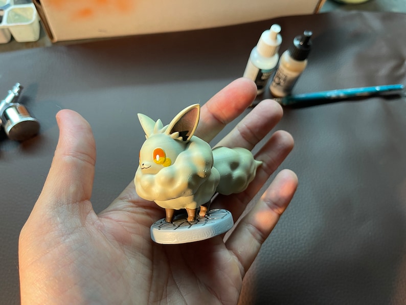May include: A white and gray Pokemon figurine of a fluffy, fox-like creature with orange eyes. The figurine is standing on a round, gray base.