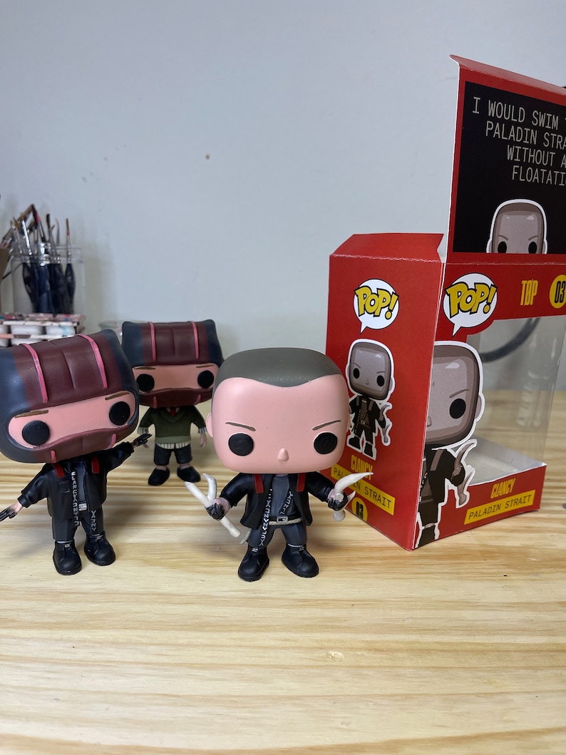 May include: Three Funko Pop figures of a character called "Clancy Paladin Strait" from the video game "The Binding of Isaac: Repentance". The figures are in a black and red box with the game's logo and the character's name. The box also has the text "I would swim to the bottom of the ocean for a Paladin Strait without a floatation device."