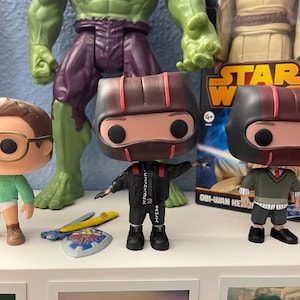 May include: Two black and red pop vinyl figures with black and white clothing. The figures are standing on a white shelf with a green Hulk figure and a Star Wars Obi-Wan Kenobi figure in the background.