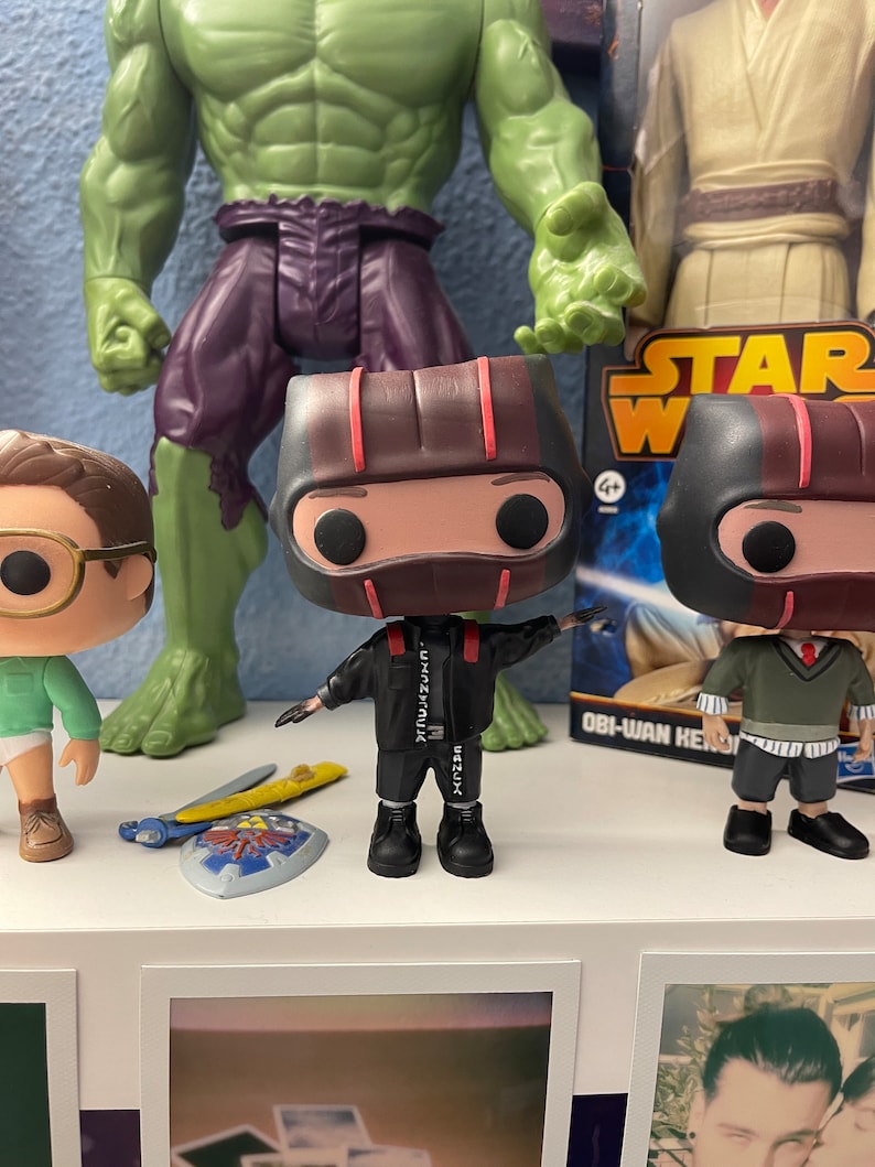 May include: Two black and red pop vinyl figures with black and white clothing. The figures are standing on a white shelf with a green Hulk figure and a Star Wars Obi-Wan Kenobi figure in the background.