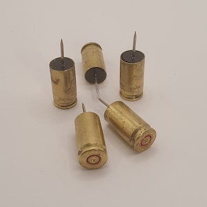 May include: Five gold bullet casings with black tops and silver pins, repurposed as push pins.