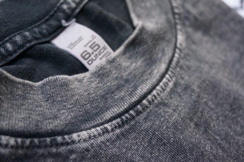 Może przedstawiać: Zbliżenie na szary t-shirt z białą metką z napisem "6.5 OUNCE" i "REPRELLE"