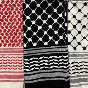 May include: Three keffiyeh scarves in red and white, black and white, and white and black. Each scarf features a distinct pattern, including a repeating geometric design and a border with a leaf-like motif. The scarves are folded and displayed side by side.