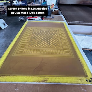 May include: A screen printing frame with a yellow border and a brown screen. The screen features a geometric pattern in yellow. Text on the image reads "Screen printed in Los Angeles on USA-made 100% cotton."