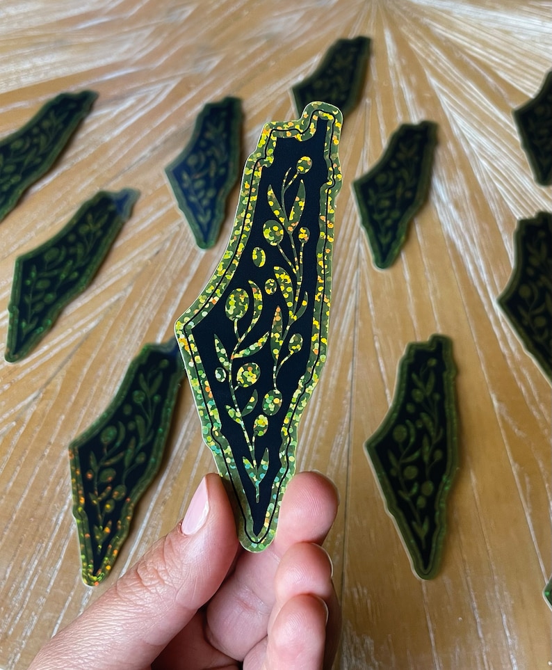 K&ouml;nnte beinhalten: Ein schwarzer und gr&uuml;ner Glitzeraufkleber mit der Umrissform Israels und einem floralen Design im Inneren.