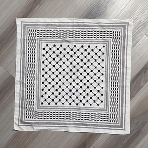 May include: Square white scarf with a black and gray geometric pattern. The scarf features a central grid of black dots, framed by borders of black and gray stripes and decorative elements. The scarf is made of a soft fabric.