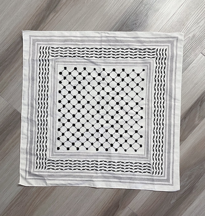 May include: Square white scarf with a black and gray geometric pattern. The scarf features a central grid of black dots, framed by borders of black and gray stripes and decorative elements. The scarf is made of a soft fabric.