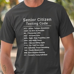 May include: Dark gray t-shirt with the text "Senior Citizen Texting Code" and a list of acronyms with their meanings. The shirt is made of a soft material.