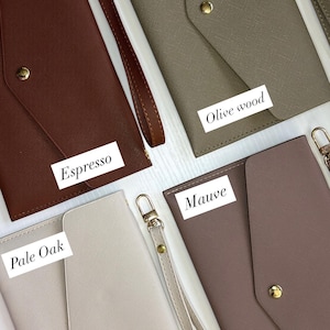 May include: Four leather clutch wallets in espresso, olive wood, mauve, and pale oak colors. Each wallet has a wrist strap and a gold-colored snap closure. The names of the colors are displayed on the wallets.