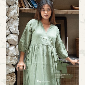 Könnte beinhalten: Ein grünes Wickelkleid mit V-Ausschnitt und 3/4-Ärmeln. Das Kleid hat einen gerafften Rock und ist aus einem leichten Stoff gefertigt. Das Kleid wird auf einem Model gezeigt, das vor einer Steinmauer steht. Der Text "Play Sewing Pattern" und "PDF Selling Pattern (A4 & A0)" ist am unteren Rand des Bildes sichtbar.