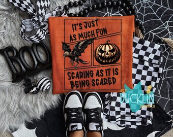 May include: Orange t-shirt with a comic book style graphic featuring a pumpkin, a bat, and the text "It's just as much fun scaring as it is being scared".