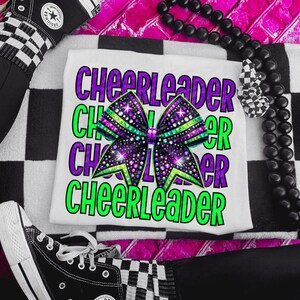 May include: White t-shirt with the word "CHEERLEADER" in purple and green, and a large bow graphic. The bow is purple, green, and black with glitter accents. Black and white checkered sneakers and socks are visible.