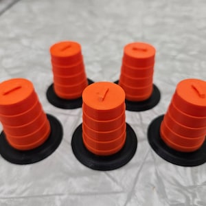 Pode incluir: Cinco cones de trânsito laranja e preto, cada um com uma base preta, estão dispostos em semicírculo sobre uma superfície cinza.