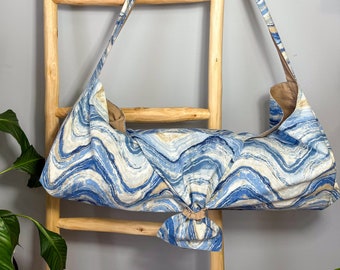 May include: A blue and white yoga mat bag with a wavy pattern. The bag is made of fabric and has a long strap that can be adjusted to fit comfortably on the shoulder.