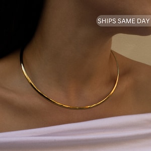 May include: A simple gold choker necklace. The necklace is made of a single, thin band of gold metal.