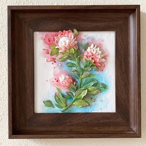 May include: A framed artwork featuring a 3D sculpted pink and white flower with green leaves against a watercolor background of pink, blue, and white.