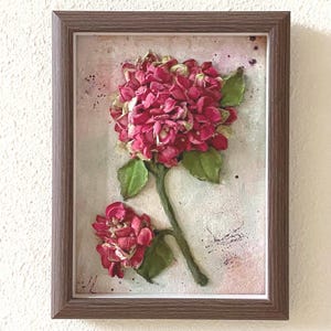 Puede incluir: Una pintura enmarcada de una flor de hortensia rosa con un fondo texturizado. La flor está en un marco marrón.