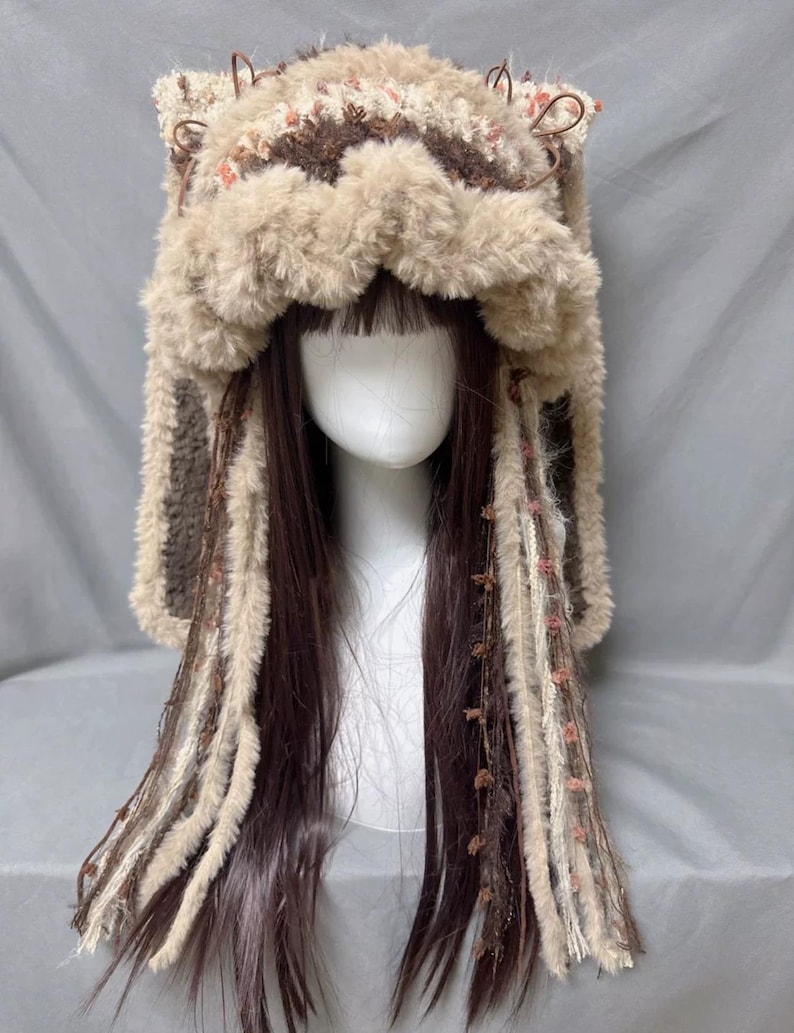 May include: A brown and beige knitted hat with furry ear flaps and long fringe. The hat has a crocheted design and is decorated with small brown beads.