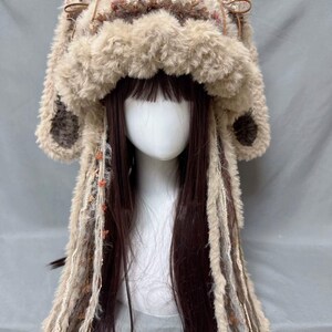 May include: A brown and white furry hat with long brown and white tassels. The hat has a large, fluffy brim and two small, furry ears.
