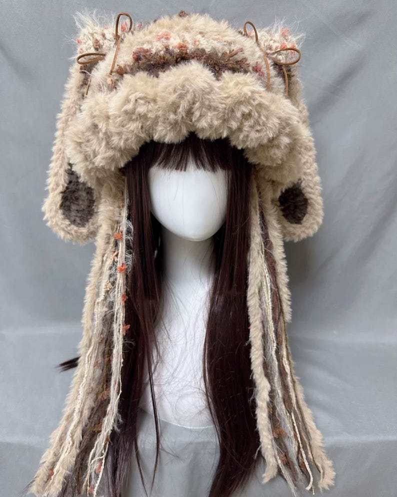 May include: A brown and white furry hat with long brown and white tassels. The hat has a large, fluffy brim and two small, furry ears.