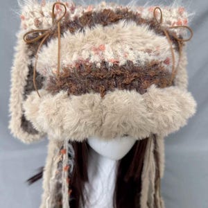 May include: A brown and white crocheted hat with faux fur trim and long brown and white yarn tassels. The hat has brown leather ties on the sides.