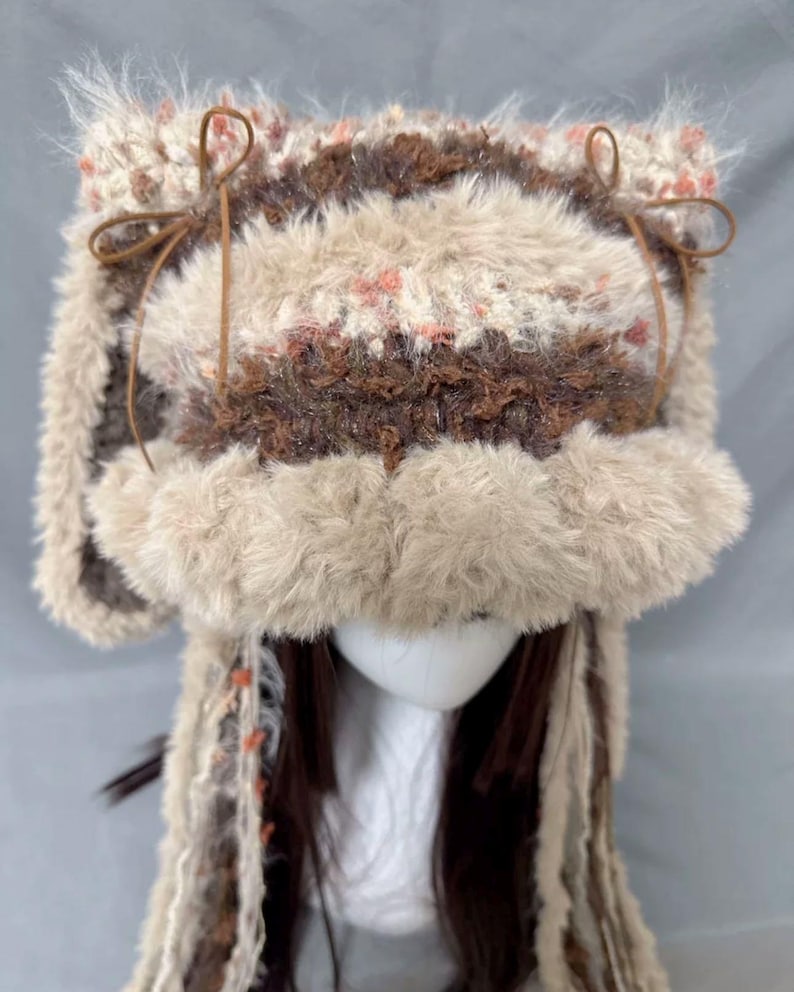May include: A brown and white crocheted hat with faux fur trim and long brown and white yarn tassels. The hat has brown leather ties on the sides.