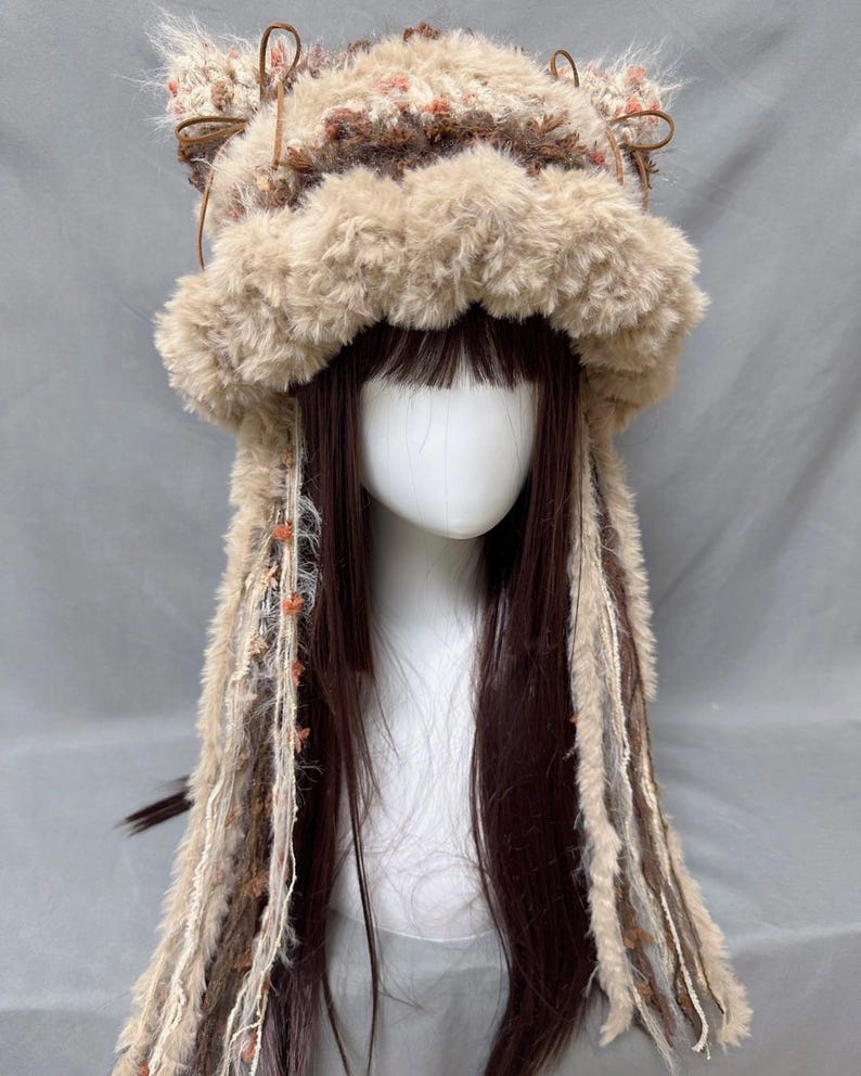 May include: A brown and beige fuzzy hat with long, brown, beige, and white yarn strands hanging down. The hat has two furry ear flaps on top.