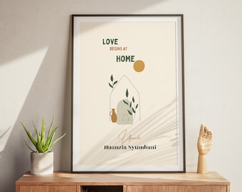 May include: A framed print with a minimalist design featuring a house with a sun and plants. The text reads "Love begins at home" and "Upendo Huanzia Nyumbani".