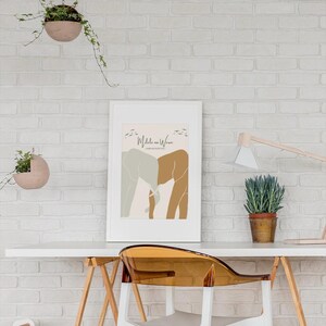 Può includere: Una stampa incorniciata bianca con un design minimalista che presenta due elefanti in tonalità di marrone e grigio, con il testo "Mdale na Wewe" e "Stronger With You" in un carattere marrone. La stampa è appesa a un muro di mattoni bianchi.